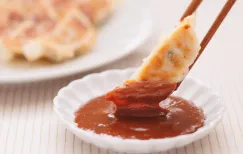Chopsticks dipping a crispy gyoza dumpling into a bowl of dedicated gyoza miso sauce
